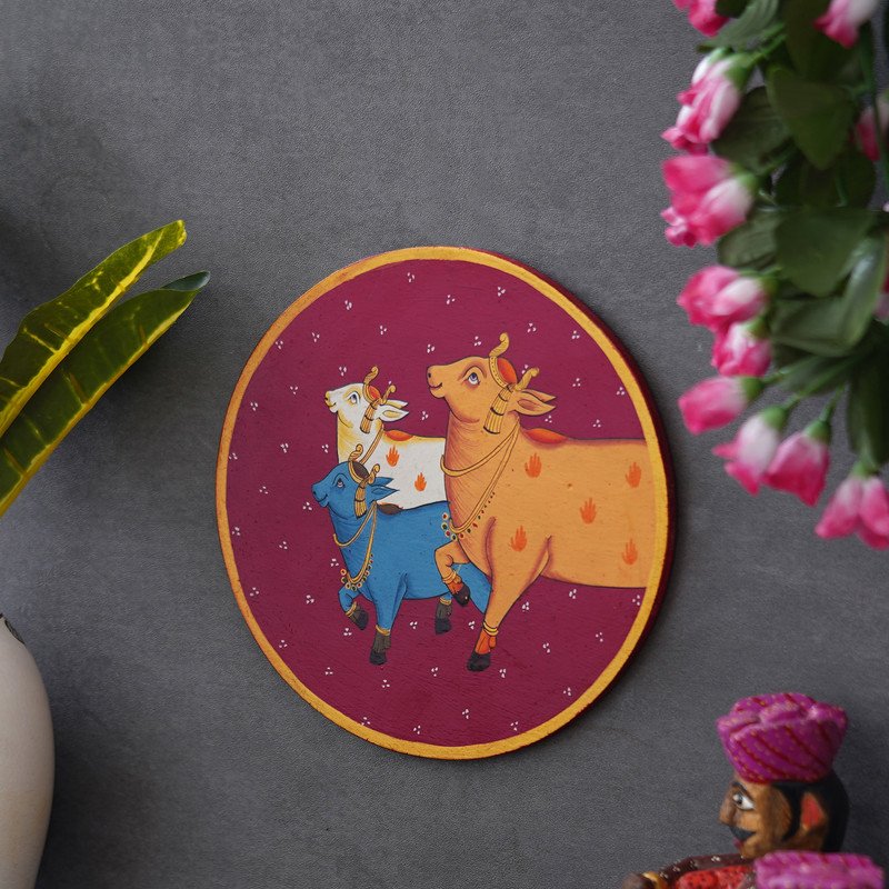 Crafted on a wooden plate, this pichwai portrays three cows in a circular formation.